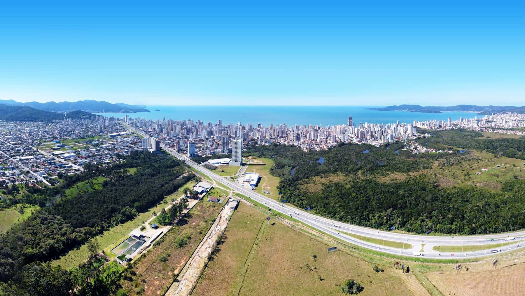 Vista aérea da região do Adonai Residence, com a BR-101, a área de preservação e a orla de Itapema e Porto Belo ao fundo