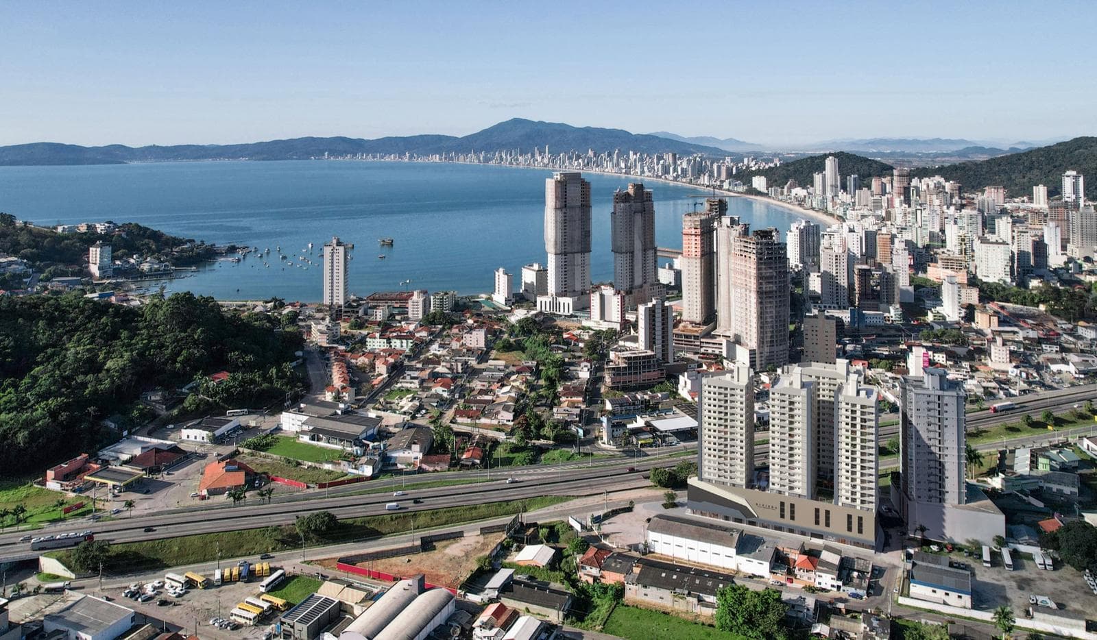 Vista aérea de Itapema, com a BR-101, os prédios do Centro e a baía ao fundo